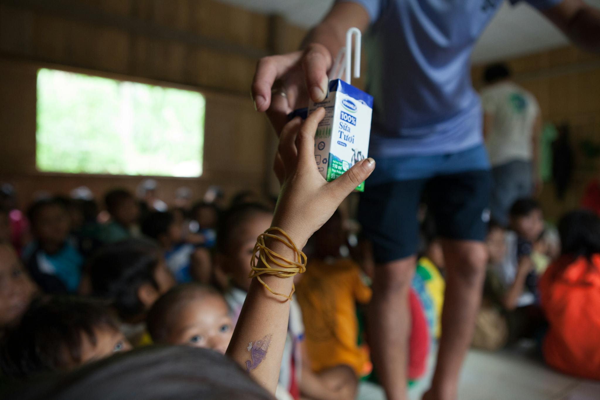 A child receives a milk carton from an adult in a busy communal room.