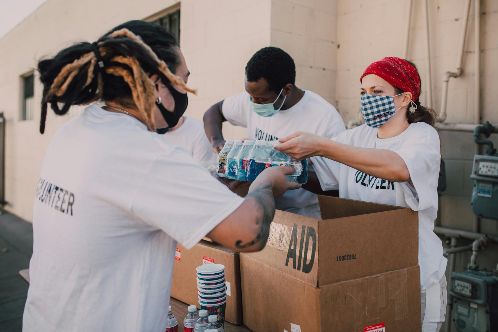 Volunteers wearing masks distribute aid boxes and water to the community outdoors.