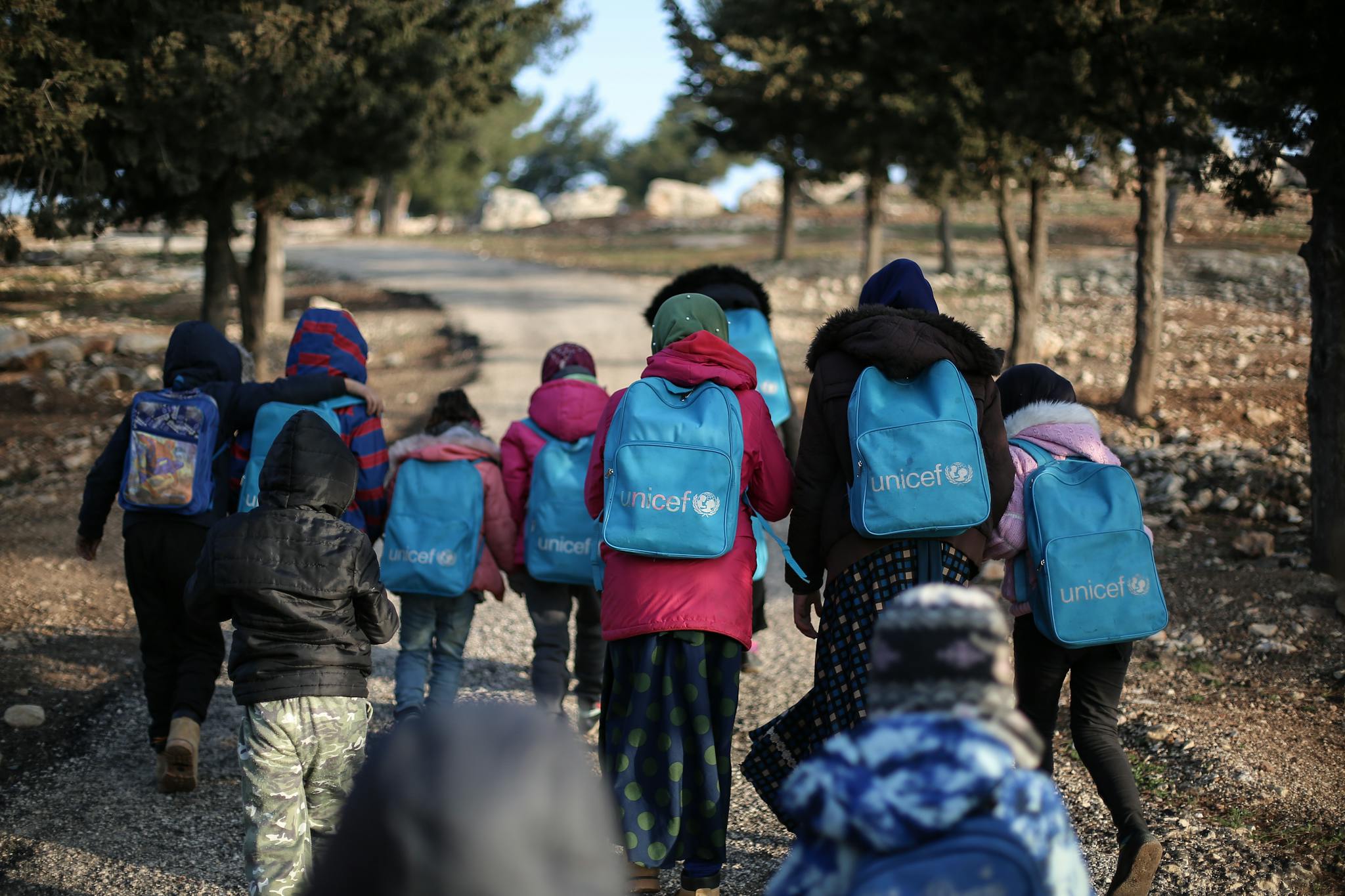 A group of children with UNICEF backpacks walking on a dirt road in rural Syria.