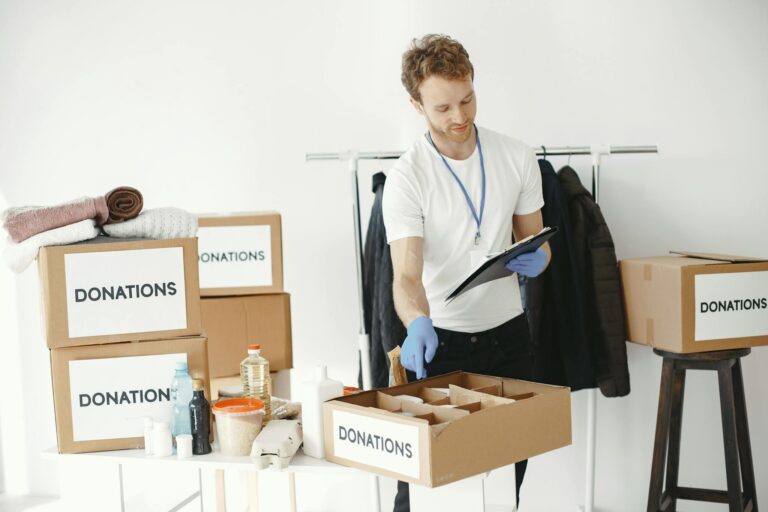A man organizing donations in boxes inside a room with various supplies on a table.