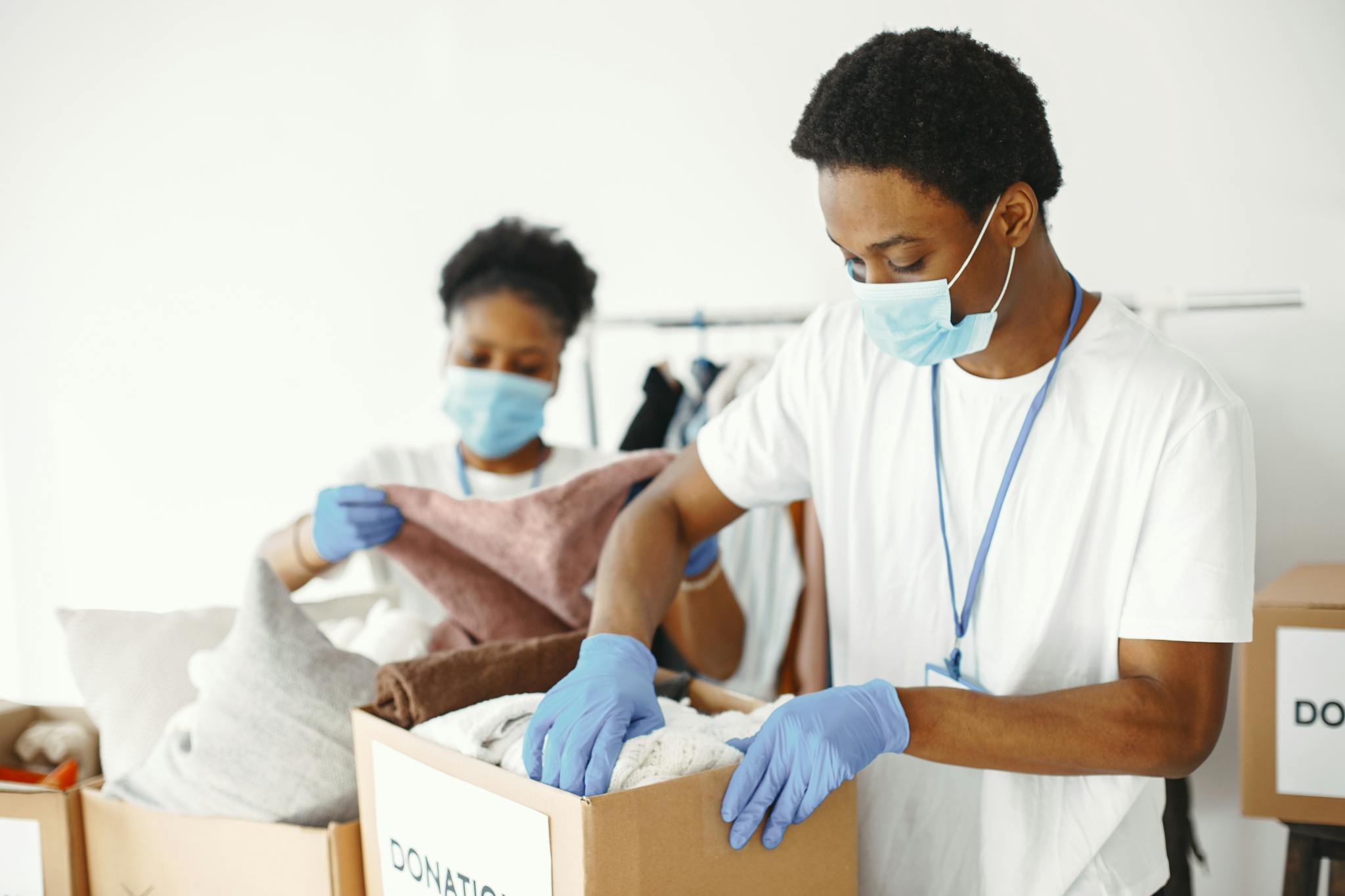 Adults wearing masks and gloves sorting donations for charity indoors.