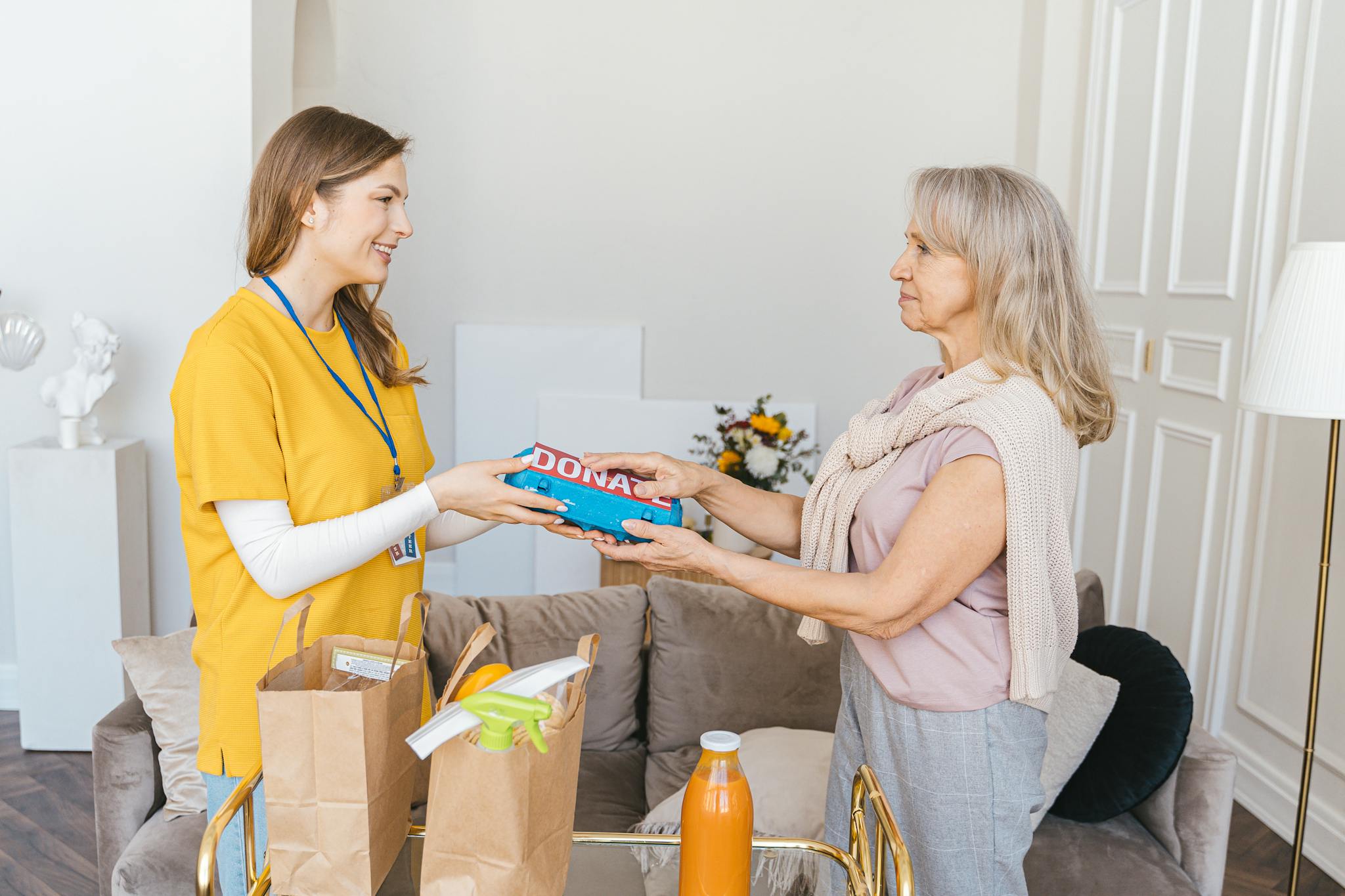 Senior woman giving donations to a smiling volunteer inside a cozy living room.