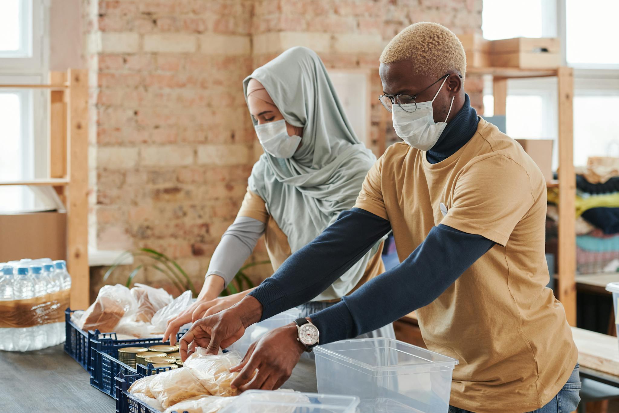 Two masked volunteers sorting and preparing food donations indoors.